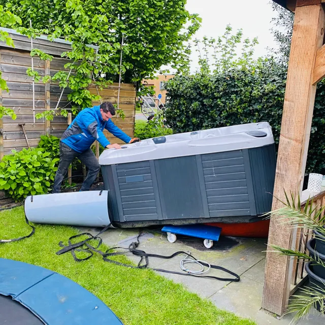 Monteur van Spaweb schuift een spa op de zijkant door de tuin