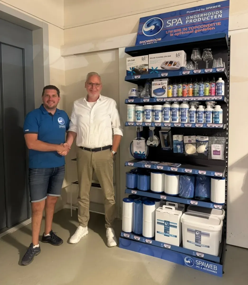 Selwin van Spaweb geeft een reseller een hand naast een stelling met Spaweb-onderhoudsproducten